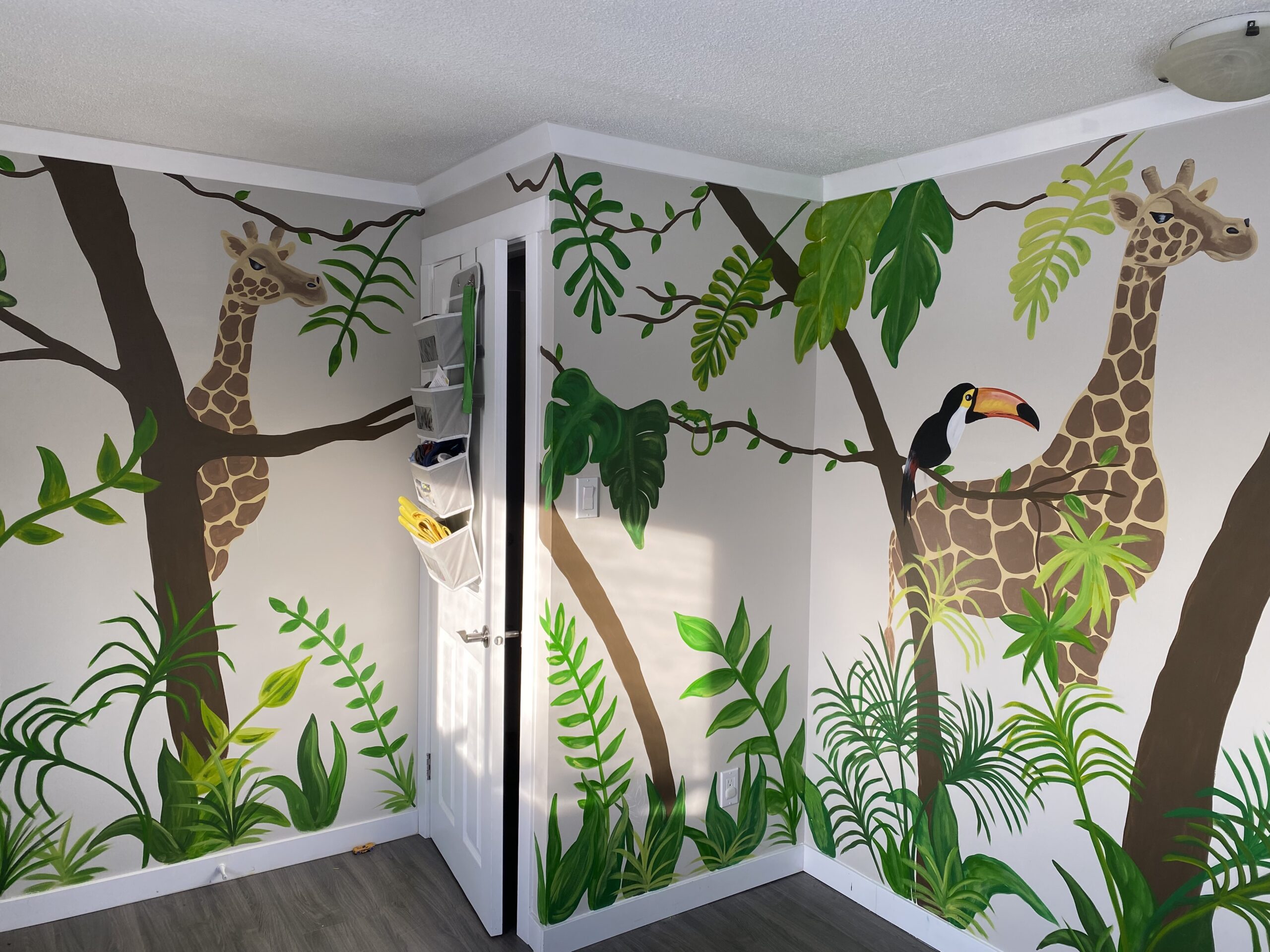 Custom painted children's safari mural hand painted by Edmonton artist Carly Marie. Covering 4 walls of a toddlers bedroom with safari animals and trees and leaves 
