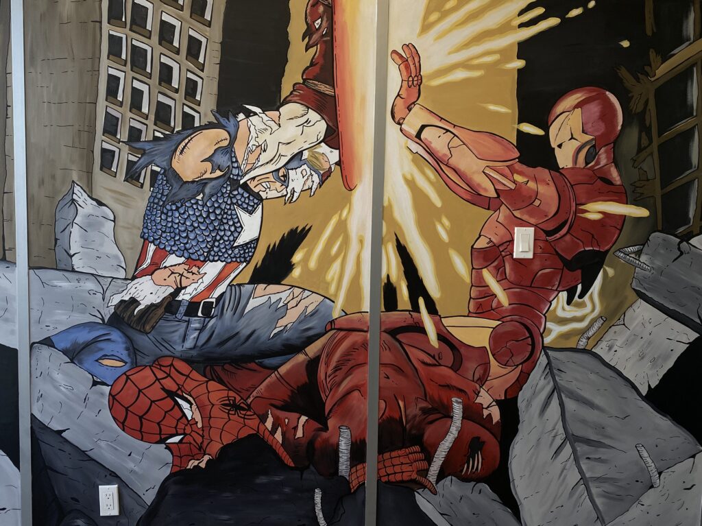 Civic War hand painted mural by Edmonton artist Carly Murray featuring Iron man, Captain America, Spider-Man, and Flash amongst the rubble painted on office wall 